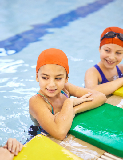 Children holding kickboards at the pool edge during a swimming lesson